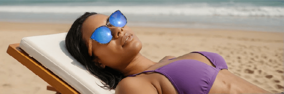 Woman lying in the sun on a beach wearing Wildwood sunglasses and smiling