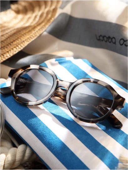 Bamburgh Sunglasses on a blue and white striped towel with a hat and rope in the background