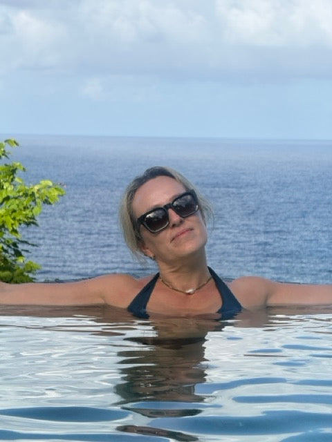 Woman in Marloes sunglasses and a swimsuit standing in water with an ocean view