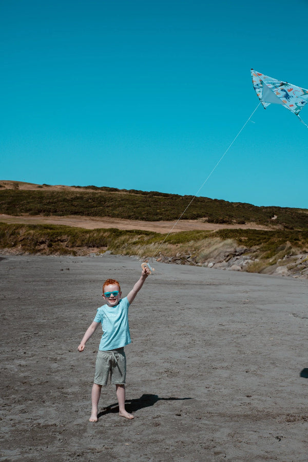 Child flying a kite on a beach with a clear blue sky