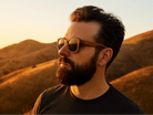 Man wearing sunglasses with a mountainous landscape in the background during sunset.