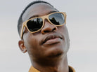 Man wearing sunglasses and a mustard yellow shirt against a light background