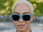 Person wearing blue sunglasses with a blurred green background