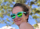 Woman wearing green reflective sunglasses with a blurred outdoor background