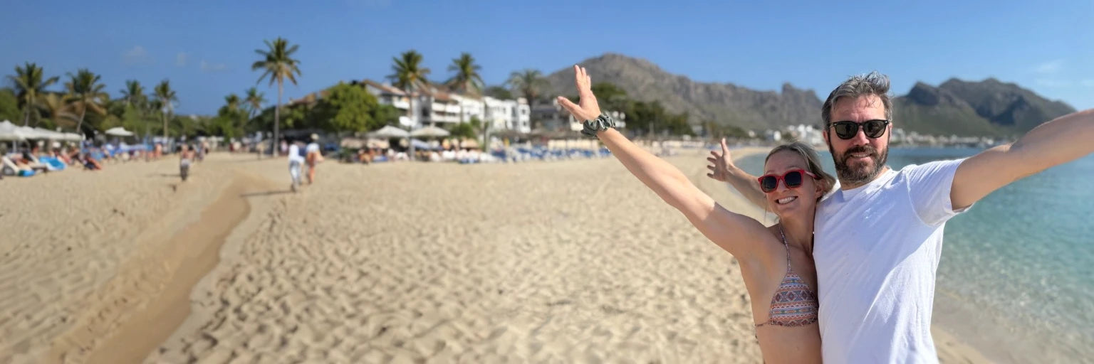Two people wearing BioSunnies on a beach with palm trees and buildings in the background
