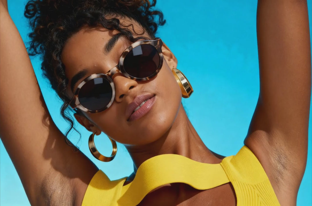 Woman dancing wearing sunglasses and a yellow top against a blue background